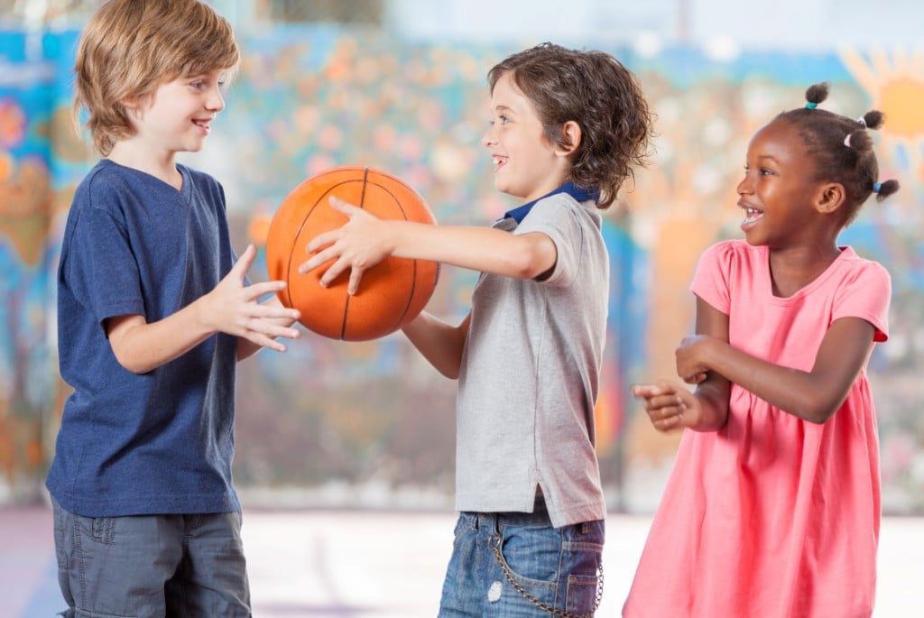 Happy multi ethnic children playing basketball at school